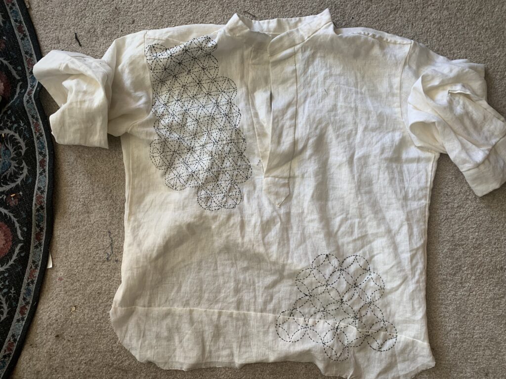 Photograph of a victorian men's shirt from above. there are two patches of sashiko embroidery on the upper left and lower right.