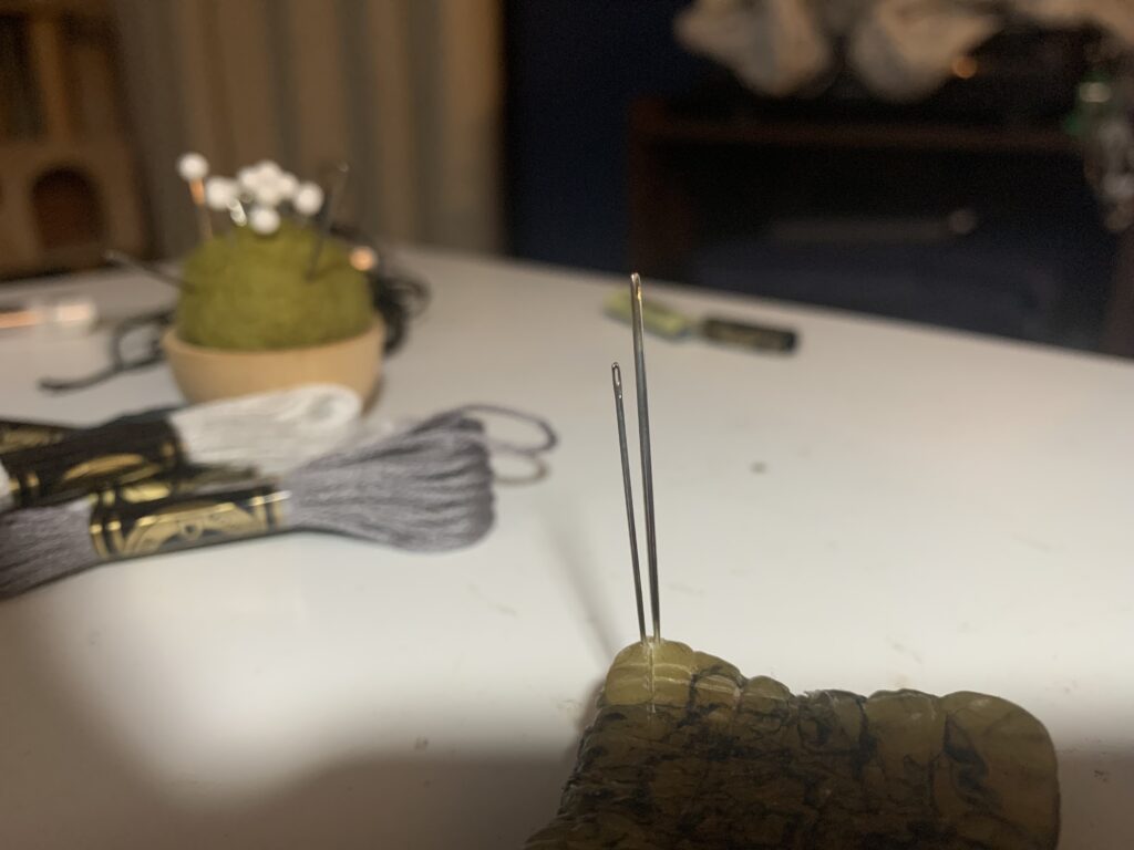 Two sewing needles embedded in a piece of wax.